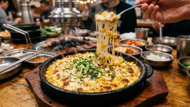 Korean corn cheese in a sizzling skillet with melted mozzarella cheese and sweet corn garnished with green onions