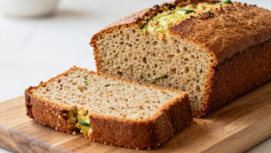 A moist slice of whole wheat zucchini bread pulled slightly forward from a loaf on a rustic wooden board.