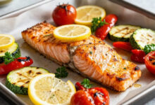 Flaky lemon herb salmon fillet roasted with vibrant vegetables on a baking sheet.